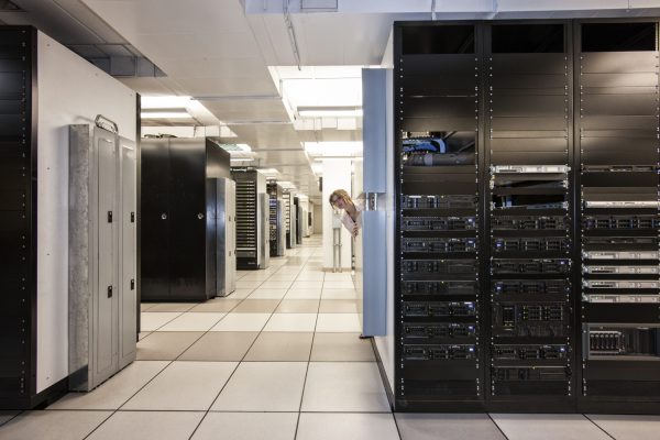 Computer server room racks with technician in background.